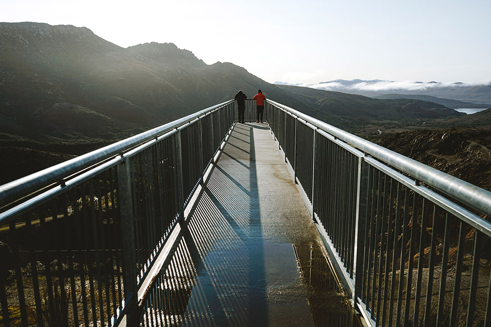 Two people at the end of a suspended walkway enjoying the distant scenery of the Iron Blow Lookout