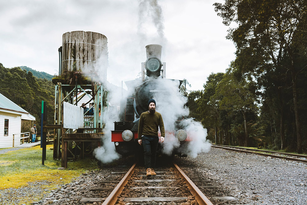 A man walking on train tracks in front of a steam train