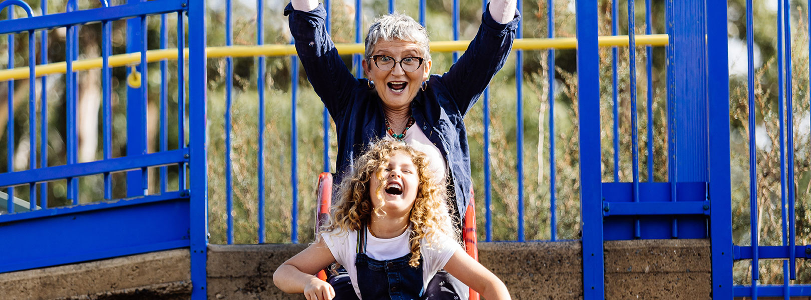 Grandma and young girl coming down a slide laughing.
