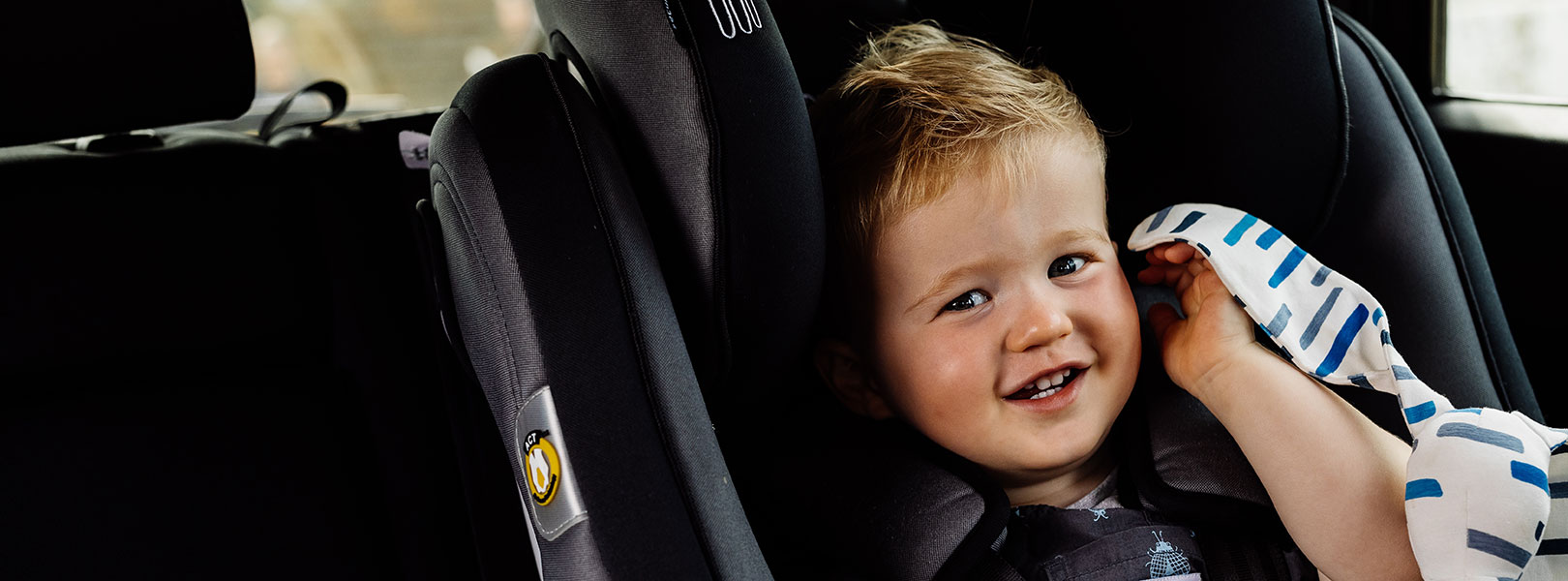 Happy toddler sitting in child seat with snuggly toy.