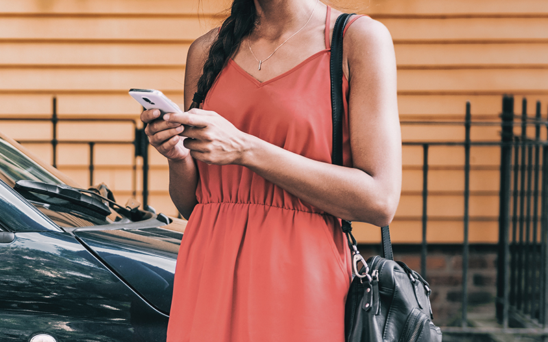 Woman using smart phone standing next to her car