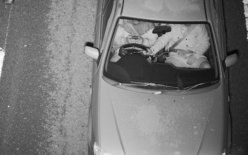 Speed camera image of passenger holding steering wheel while driver is texting
