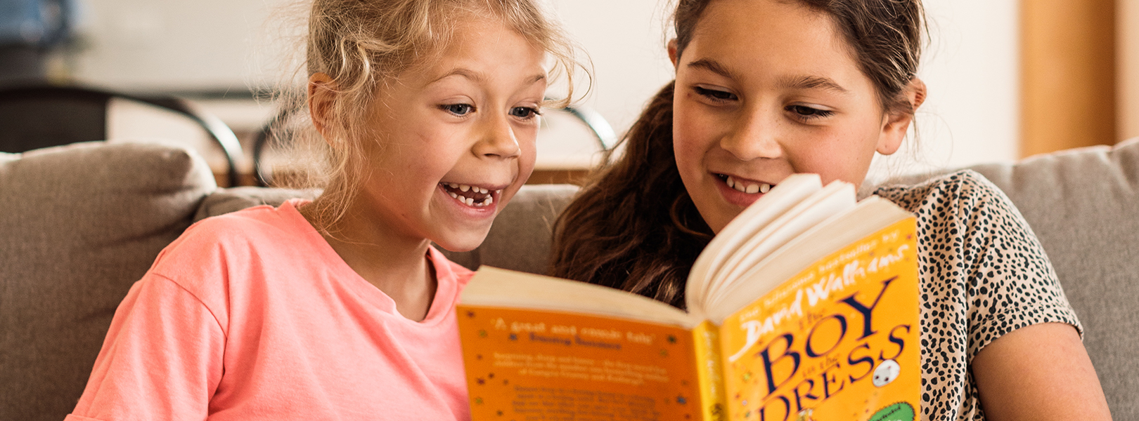 Two young girls reading a book on the couch