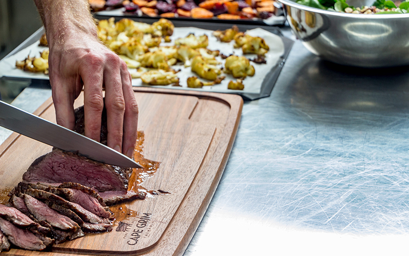 Slicing cooked beef on a wooden chopping board