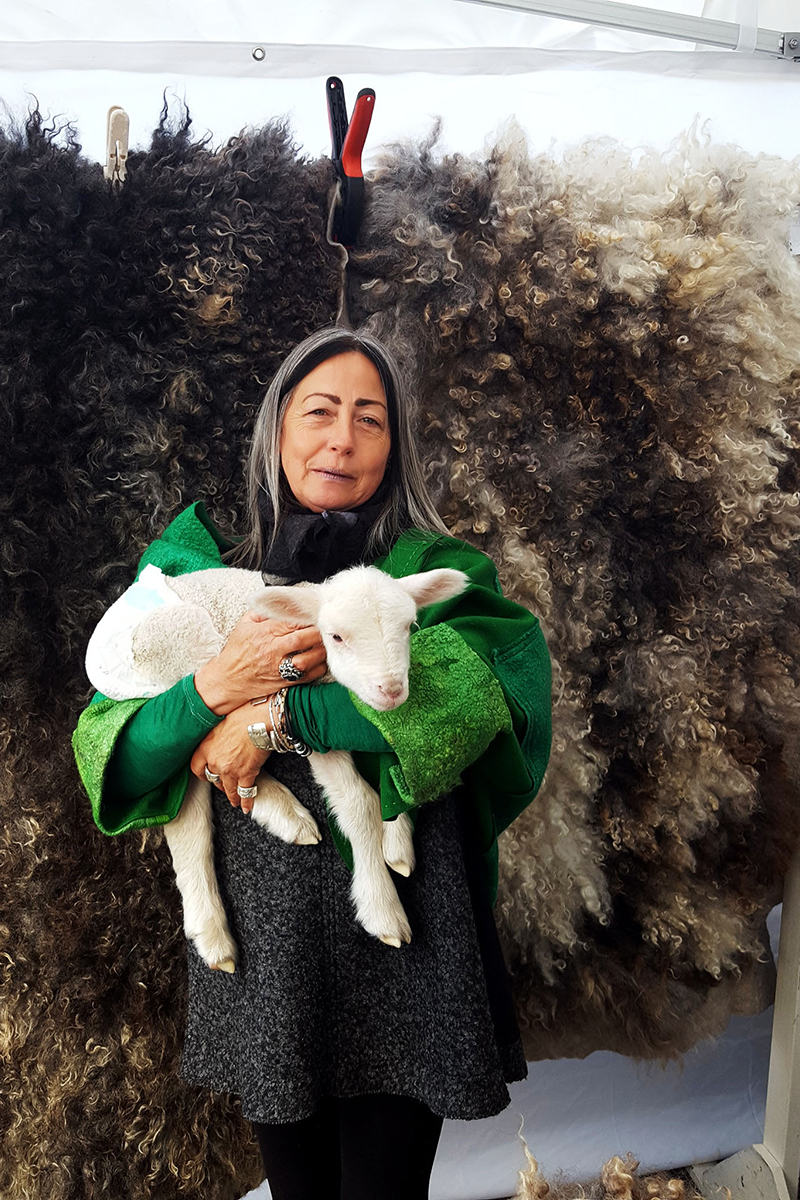 Rebecca Kissling holding a lamb in front of a wool textile