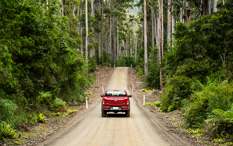 Red Mazda BT-50 ute driving down a dirt road