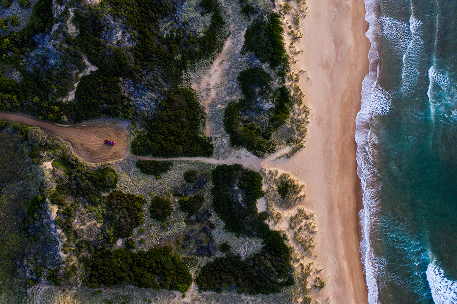 Aerial view of waves, beach, bush and the red Mazda BT-50