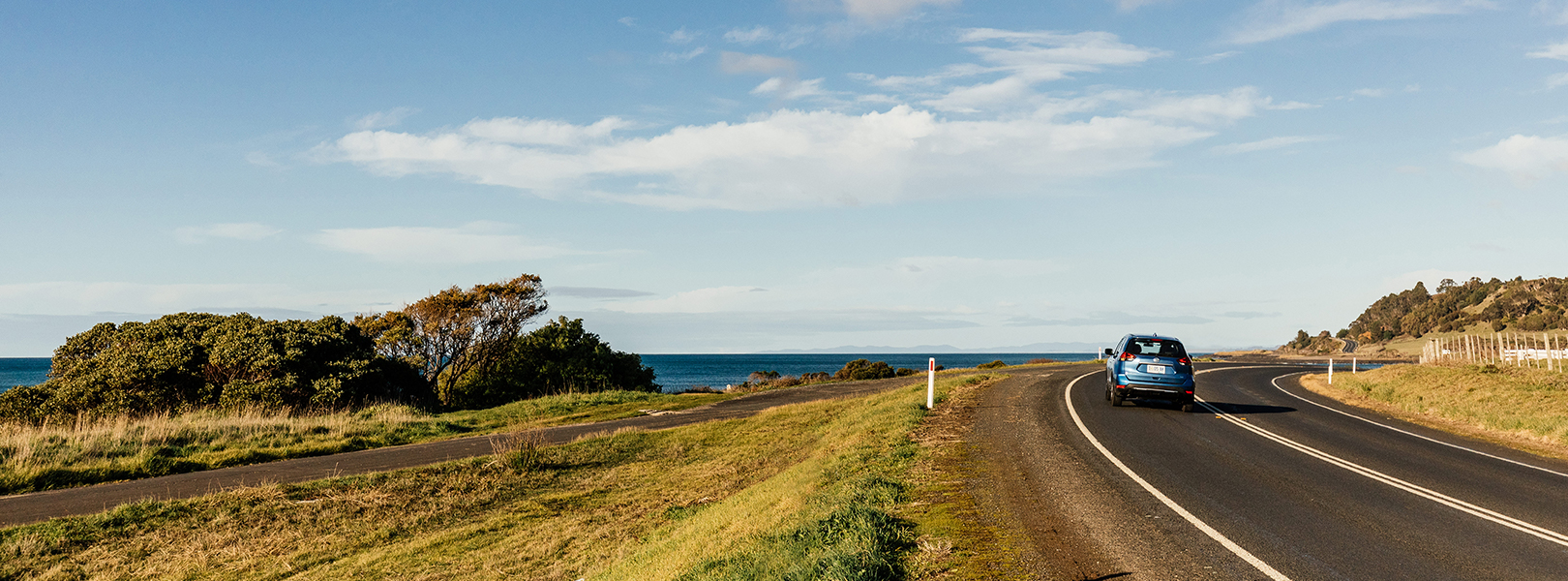 Blue car driving on coastal road