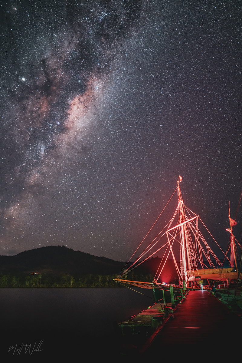 The Milky Way above a glowing red boat