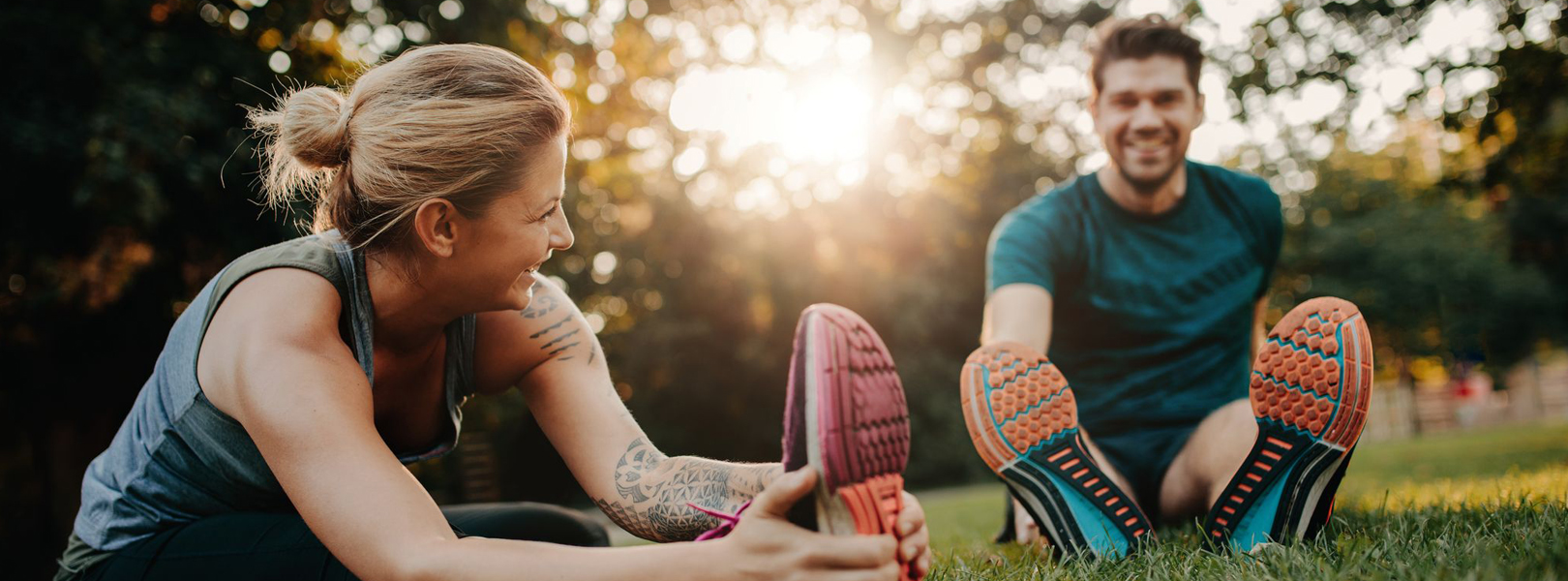 Female and male wearing gym clothing stretching on grass in sunshine